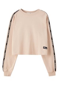 Sweat-shirt court beige à manches longues avec un ruban noir le long des manches indiquant "New Challenges" et un petit patch avec le même texte près de l'ourlet.