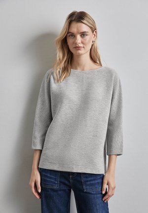 Hellgrauer, strukturierter Pullover mit weitem Ausschnitt und Dreiviertelärmel, kombiniert mit dunkelblauen Jeans. Schlichte, lockere Silhouette.