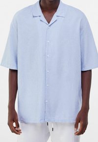 Modrá a bílá pruhovaná košile s krátkým rukávem, uvolněný střih, zapínání na knoflíky a límečkový výstřih. Měkká textura s vertikálním pruhovaným vzorem.