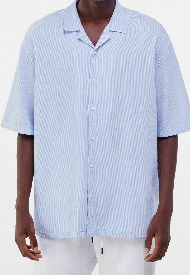 Modrá a bílá pruhovaná košile s krátkým rukávem, uvolněný střih, zapínání na knoflíky a límečkový výstřih. Měkká textura s vertikálním pruhovaným vzorem.