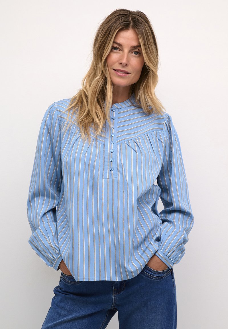 Blusa a manica lunga azzurro chiaro con strisce verticali bianche e dorate, colletto e sette bottoni frontali. Vestibilità rilassata con dettagli plissettati.