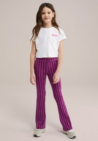 Valge lühikeste varrukatega T-särk roosa tekstiga ja lillaga triibulised laiendatud retuusid. Retuusidel on vertikaalsed triibud ja sile tekstuur.