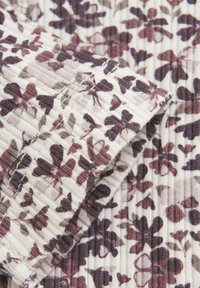 Rippstoff mit floralem Muster in Dunkellila und Burgunder auf einem cremefarbenen Hintergrund, mit sichtbaren Nähdetails.