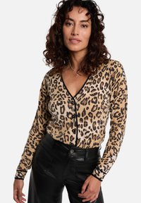 Luipaardprint cardigan in beige en zwart, met een diepe V-hals, knoopsluiting en lange mouwen. Gecombineerd met zwarte leren broek.