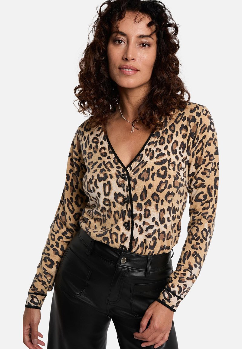 Luipaardprint cardigan in beige en zwart, met een diepe V-hals, knoopsluiting en lange mouwen. Gecombineerd met zwarte leren broek.