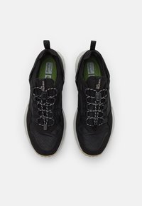 Scarpe da allenamento nere con superficie testurizzata, sistema di lacci elastici e plantari verdi. Presentano un design leggero e suole in gomma grigia.