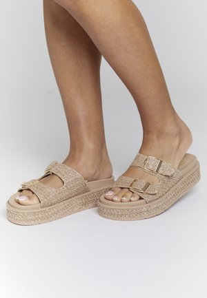 Beige platform sandals with woven upper, dual buckle straps, and textured sole. Open toe design highlights pedicure. Flat heel.