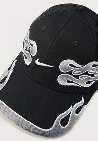 Czarna czapka bejsbolówka z haftowanymi srebrnymi wzorami płomieni i białym logo Nike na przodzie. Materiał o fakturze z zakrzywionym daszkiem.