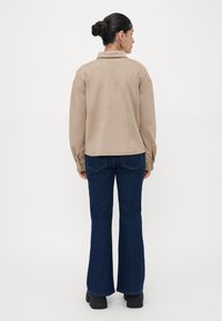 Beige suede shirt jacket with a folded collar, single-button cuffs, and blue flared jeans, paired with black platform boots.
