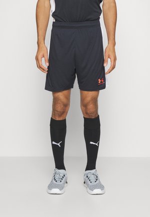 Czarne sportowe szorty z elastycznym paskiem w talii oraz pomarańczowym logo Under Armour. Połączone z czarnymi skarpetkami do kolan z białym logo Puma.