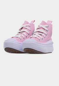 Ροζ ψηλά αθλητικά παπούτσια με λευκά κορδόνια και χοντρές λευκές σόλες, εμφανιζόμενα από χαμηλή μπροστινή γωνία σε λευκό φόντο.