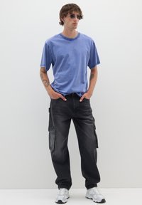 Blauwe crew neck t-shirt met korte mouwen, gecombineerd met zwarte cargo broeken met meerdere zakken, en witte sneakers.