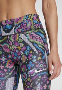 Leggings de Nike coloridos con una base negra y patrones geométricos intrincados en rosa, azul, verde y amarillo. Textura suave con cintura alta.