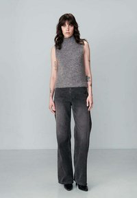 Grijze mouwloze gebreide top met een hoge hals, gecombineerd met hoge, donkere grijze flared jeans en zwarte schoenen. Soepele textuur.