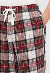 Kockás pizsamanadrág piros, zöld és tengerészkék színben, krémszínű háttéren. Rugalmas derékpánttal rendelkezik, fehér húzózsinórral és oldalsó zsebekkel.