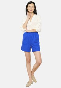 Gaišs viegls baltas blūze ar ziedu izšuvumu, apvienota ar līdzceļa garuma ziliem lina šortiem ar elastīgu jostasvītru un divām priekšējām kabatām.