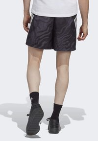 Shorts sportivi neri con un motivo testurizzato, dotati di tre strisce bianche sui lati. Indossati con calze e scarpe nere, mostrando gambe nude.