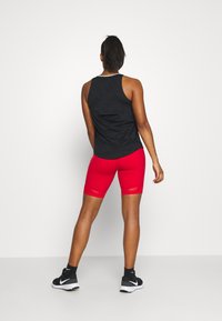 Svart sporttopp och röda cykelshorts, sömlös design, figurnära passform, mjukt material, bärs med svarta träningsskor och ankelsockor.