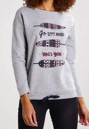 Grauer Pullover mit Rundhalsausschnitt. Verziert mit drei gemusterten Federn in Rot, Blau und Weiß sowie dem Text: "Geh, wohin dich der Wind trägt."
