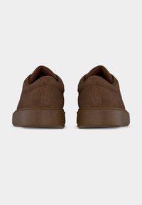 Ζευγάρι καφέ σουέντ αθλητικά παπούτσια που φαίνονται από πίσω με χοντρές καφέ σόλες στον ίδιο χρωματισμό πάνω σε λευκό φόντο.