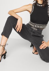 Top sin mangas negro con tachuelas en forma de diamante, combinado con pantalones grises y tacones negros con tiras que presentan acentos redondos.
