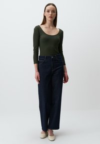 Body a maniche lunghe verde a coste abbinato a jeans high-waisted blu scuro, con una vestibilità comoda e tasche laterali. Le scarpe color cuoio completano il look.
