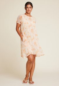 Blomstermønster kjole i lys fersken med korte puff ermer, med sidelommer og løs A-linje form. Mykt, gjennomsiktig stoff med rose mønster.