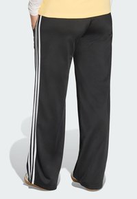 Black athletic pants with white stripes down the sides, made of smooth material, featuring a relaxed fit and pockets on both sides.