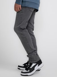 Vaqueros de mezclilla gris con un corte ajustado y bolsillos frontales, combinados con zapatillas deportivas en blanco y negro con un diseño de caña alta.