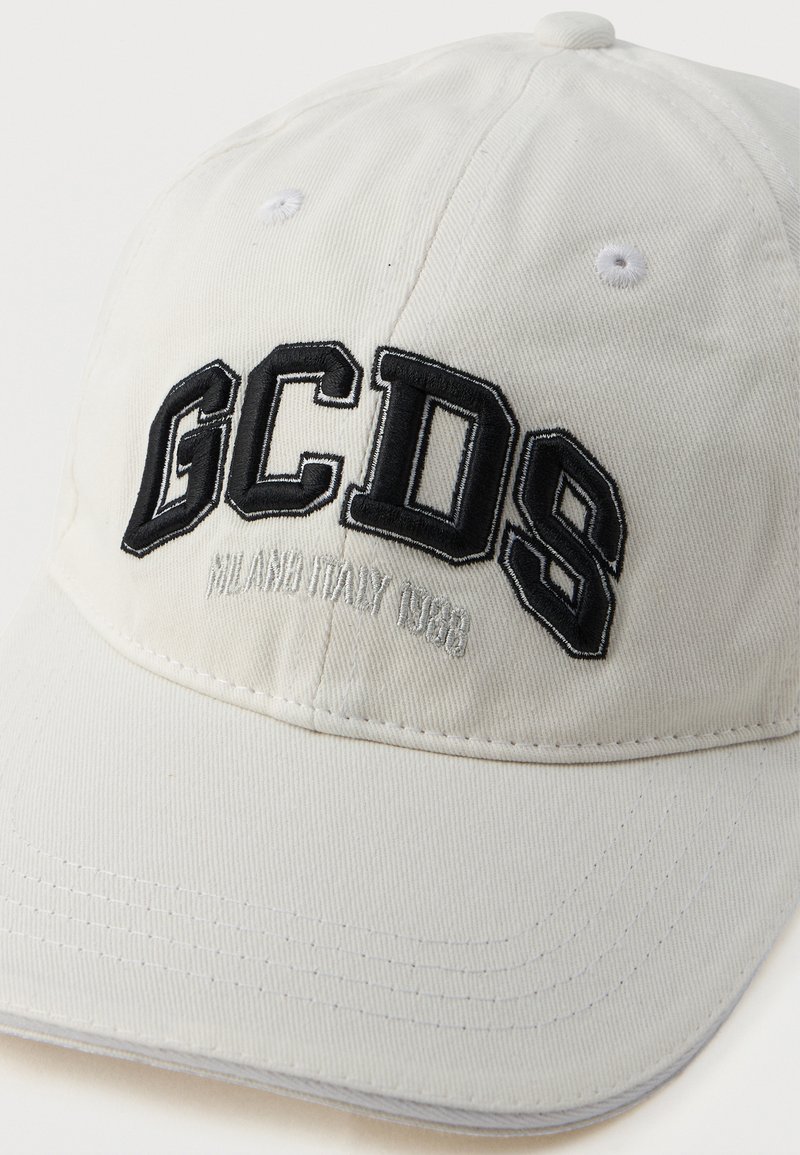 Casquette de baseball en coton blanc avec un logo "GCDS" noir brodé. Présente le texte "MILAN ITALIE 1983" et six panneaux avec des détails de couture.