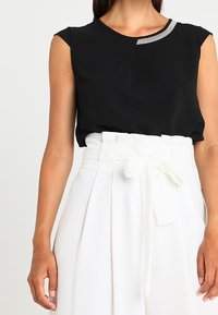 Top negro sin mangas con un escote redondo y un acento gris. Combinado con una falda blanca de cintura alta, adornada con un lazo y pliegues.