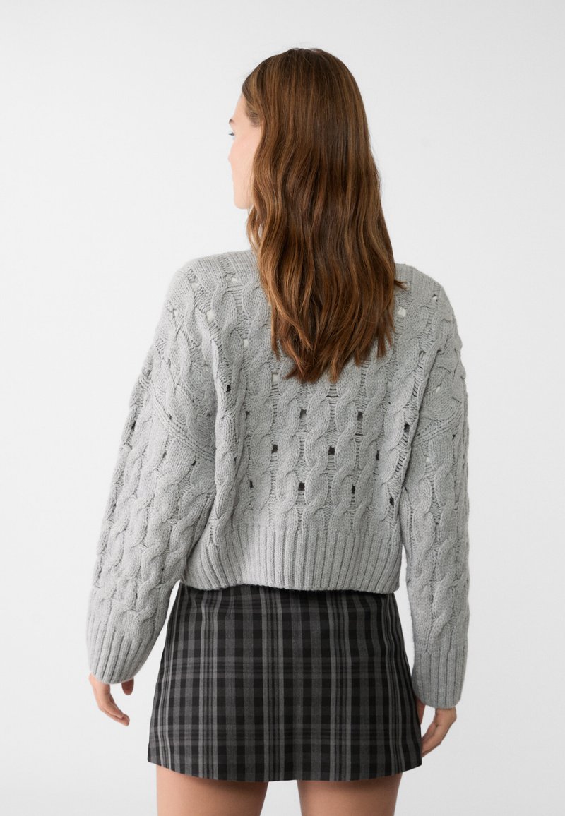 Maglione grigio a maglia con motivo a trecce, dotato di maniche fluide, abbinato a una mini gonna a quadri nera. Texture liscia, design corto.