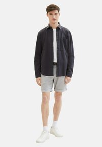 Camisa azul marino de botones con un bolsillo en el pecho, combinada con pantalones cortos de cuadros grises. Una camiseta blanca debajo y zapatillas blancas completan el conjunto.