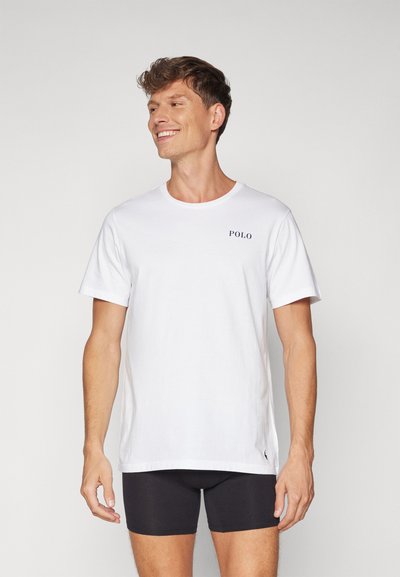 Biela bavlnená tričko s okrúhlym výstrihom, krátkymi rukávmi a logom "POLO" v námorníckej modrej na hrudníku. Nosené s čiernymi boxerami.