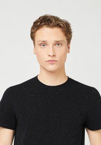 Schwarzes kurzärmliges T-Shirt mit gepunktetem Muster, Rundhalsausschnitt und kleiner Brusttasche. Hergestellt aus einem Baumwollmischgewebe mit glatter Textur.