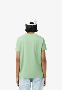 Lichtgroene katoenen T-shirt met korte mouwen, ronde halslijn en een naadloze achterkant. Accentueert met een wit verstelbaar baseballpet.