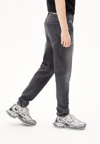 Donkergrijze denim jeans met een slim fit, voorzien van achterzakken en contrasterende stiksels. Draagt met grijze en witte sneakers.
