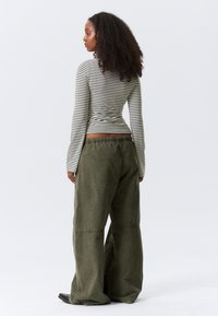 Črtasta majica z dolgimi rokavi v beli in zeleni barvi; kombinirana z širokimi olivno zelenimi hlačami; teksturirana tkanina; elastičen pas; sproščen kroj.