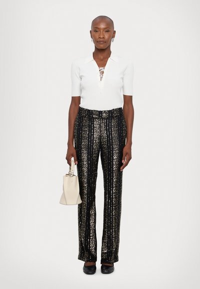 White ribbed polo top with short sleeves and lace-up detail, paired with black and gold patterned flared trousers; holding a small beige bag.