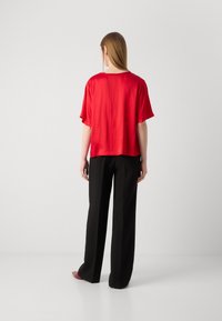 Top corto a maniche corte in satin rosso con vestibilità ampia, abbinato a pantaloni neri a vita alta. Tessuto liscio e silhouette rilassata.