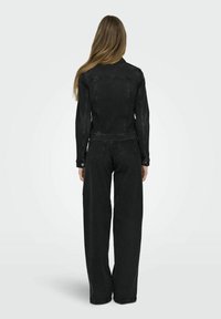 Svart denimjacka och byxset, med en figurnära jacka med långa ärmar och vida byxor. Texturerat tyg med kontrasterande sömmar.