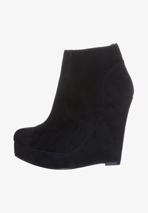 Botín de ante negro con cuña, que presenta una textura suave, un diseño curvado y una suela tipo plataforma. La vista lateral no muestra cierre de cremallera.