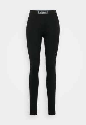 Leggings noirs en tissu extensible, avec une taille haute élastique arborant un label logo blanc, au design ajusté et à la texture lisse.