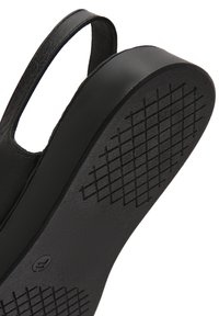 Zapato de cuero negro con punta redondeada, parte trasera abierta y suela de goma texturizada que presenta un patrón de rejilla para mayor agarre y tracción.