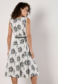 Vestido floral con fondo blanco y patrones de rosas negras, diseño sin mangas y cintura entallada con un cinturón negro de acento.