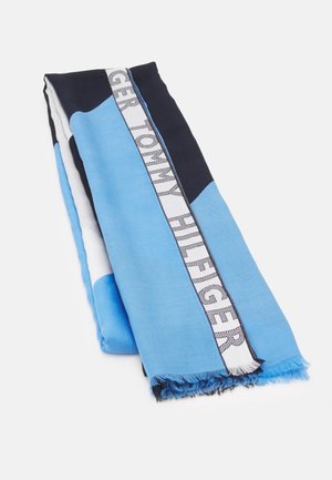 Złożony niebiesko-czarny szalik z frędzlami i białym paskiem z napisem "Tommy Hilfiger" w szarych literach.