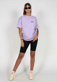 Lilla bomulds T-shirt med korte ærmer og en lille sort grafik på fronten, parret med sorte cykelshorts og beige høj-top sneakers.