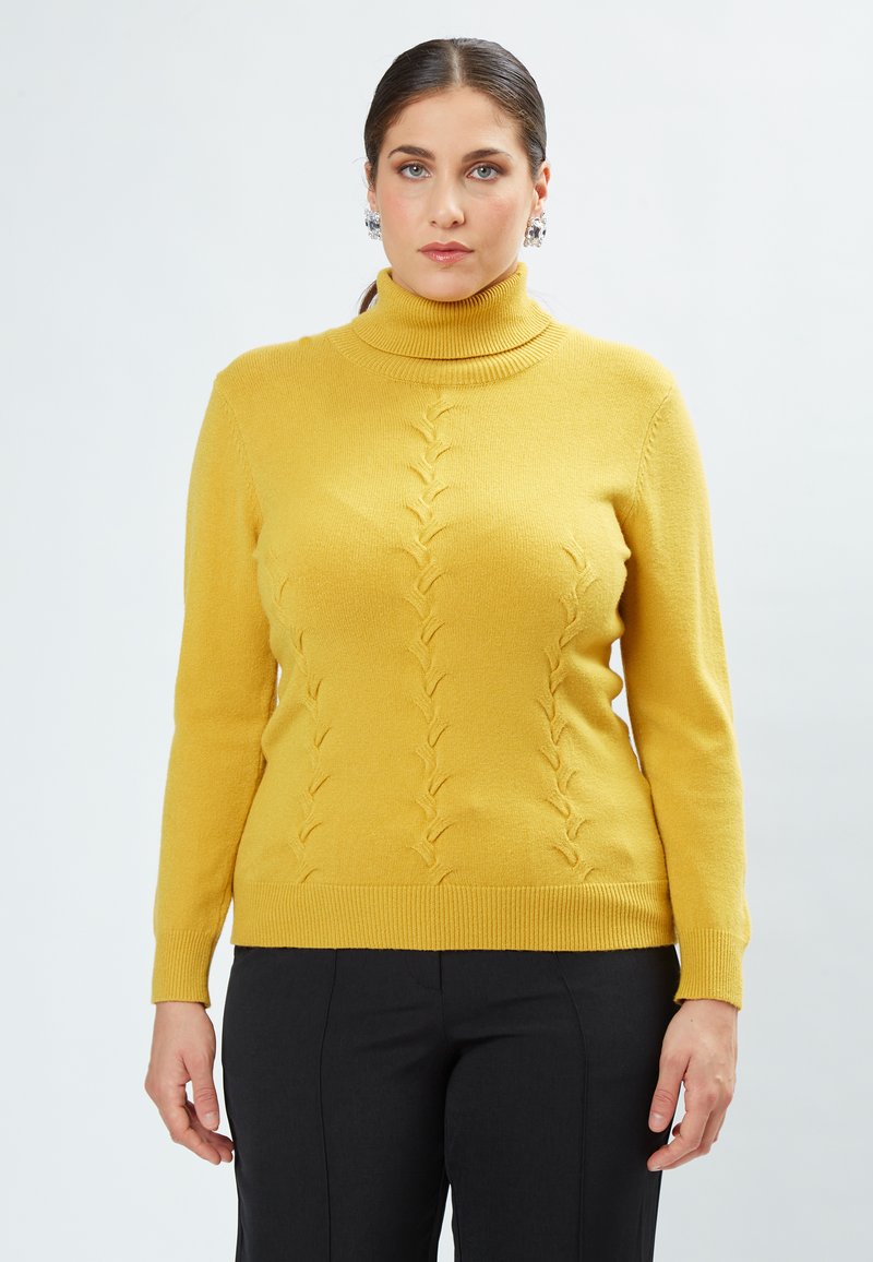 Suéter amarillo de cuello alto con un patrón texturizado de puntos elevados, dobladillo y puños acanalados, combinado con pantalones oscuros.