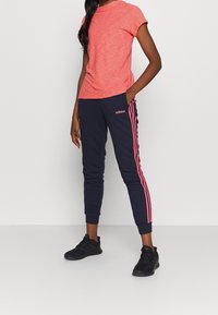 Červené melírované tričko s kulatým výstřihem v kombinaci s námořnickými tepláky s růžovými bočními pruhy a logem adidas, doplněné černými teniskami.