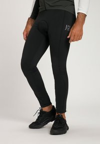 Schwarze Sportleggings mit einer enganliegenden Passform, die eine Naht entlang des Beins und ein rundes Polsterdetail aufweisen. Glänzendes Logo nahe dem Oberschenkel.